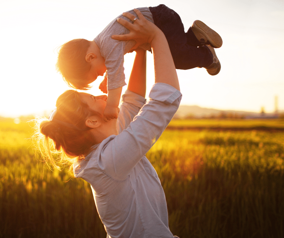 mother holding child above her head on a field during sunset