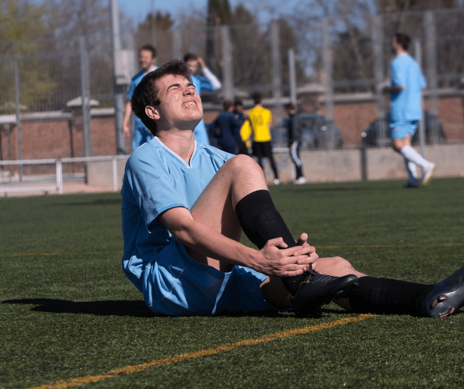 man sitting on ground holding his ankle and crying
